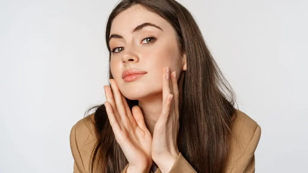 botox or filler. Beauty and skin care. Close up portrait of beautiful woman looking in mirror and touching her clear glowing face, standing over white background
